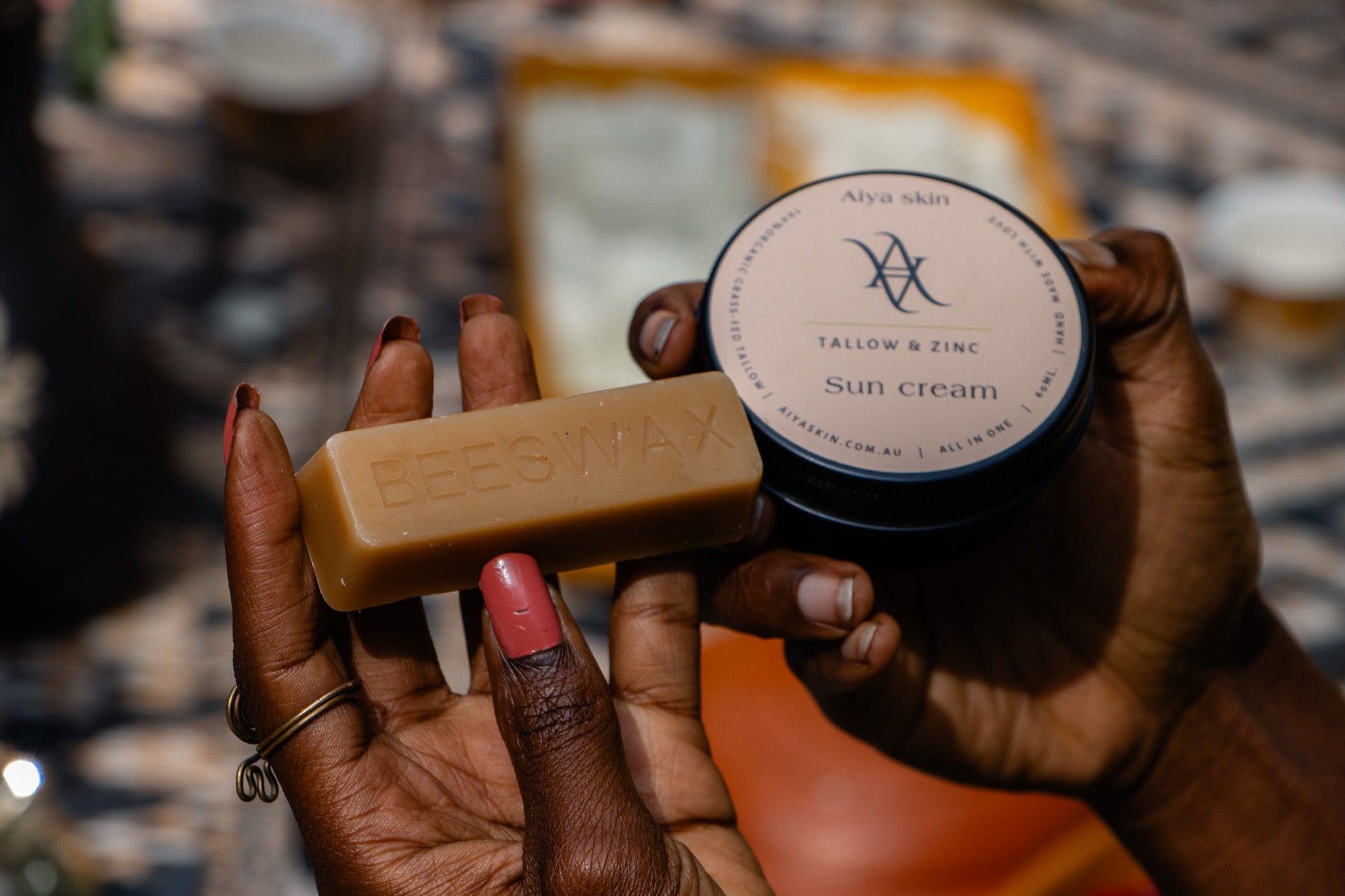 Hand holding a bar of boos wax and a container of sun cream with visible branding.